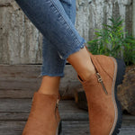 Brown suede boots with zippers worn with blue jeans against a rustic background