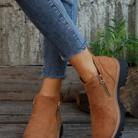 Brown suede boots with zippers worn with blue jeans against a rustic background