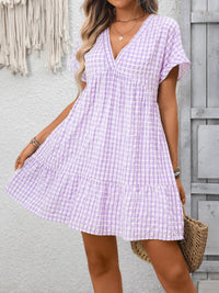 Woman wearing a purple checkered dress against a gray wall.