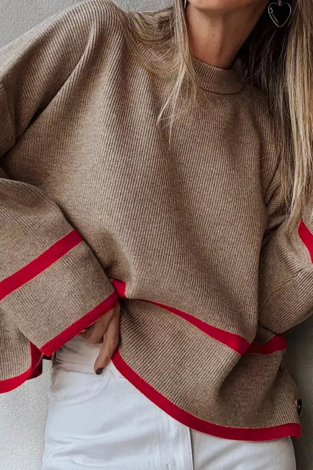 Beige sweater with red trim worn by a person, with a neutral background