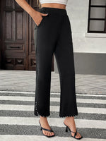 Person wearing black wide-leg pants with a white building and wooden door in the background