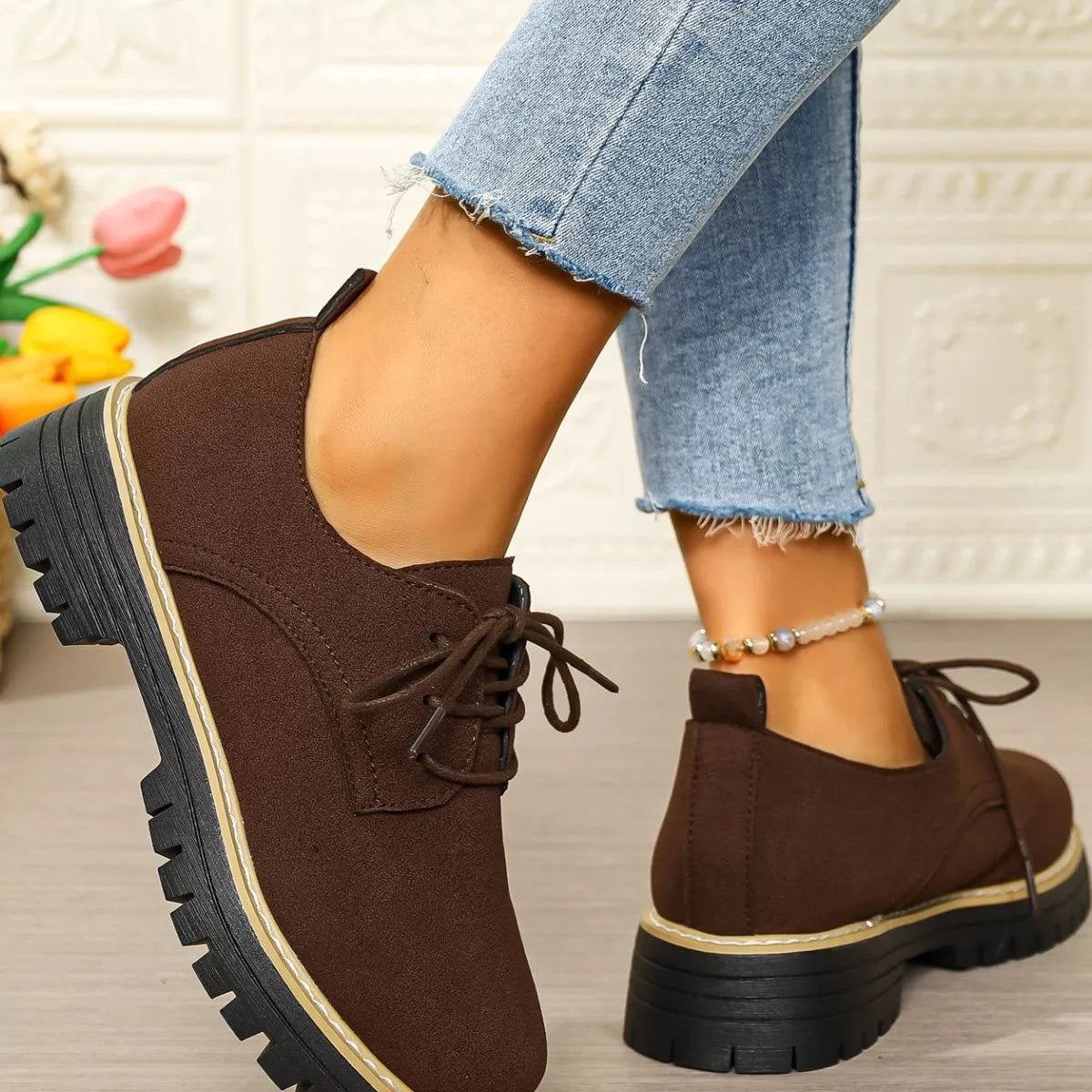 Brown shoes with black soles worn by a person with light blue jeans.