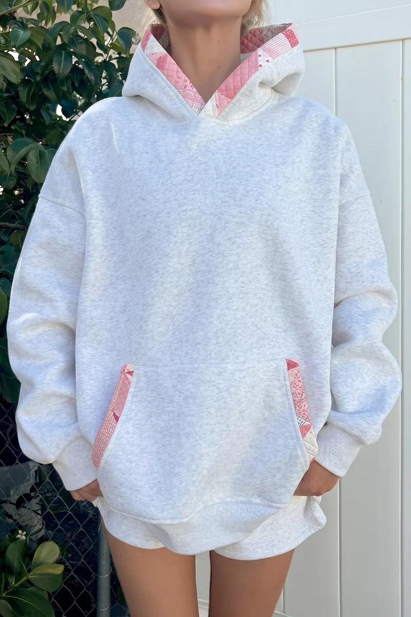 Person wearing a light gray hoodie with pink lining in an outdoor setting