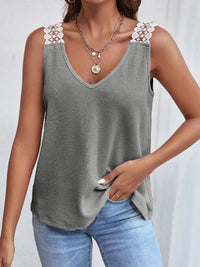 Woman wearing a gray tank top with floral straps and blue jeans on a white background