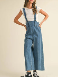 Person wearing blue denim overalls on a plain background