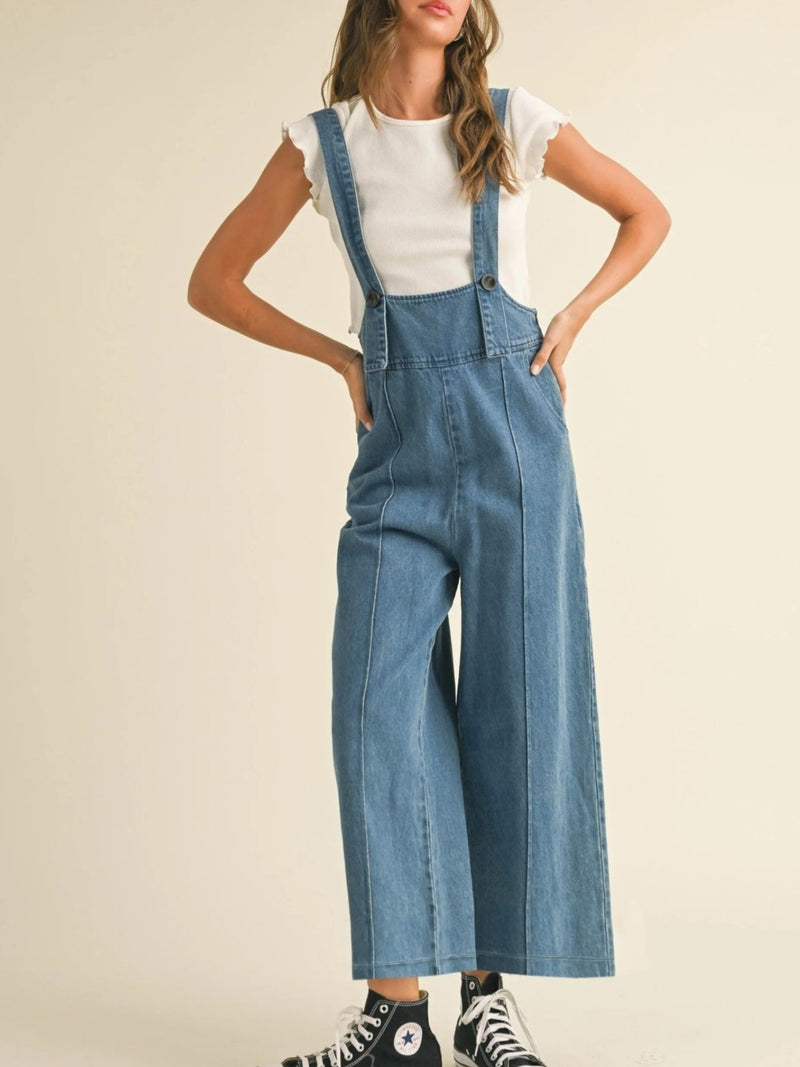 Person wearing blue denim overalls on a plain background