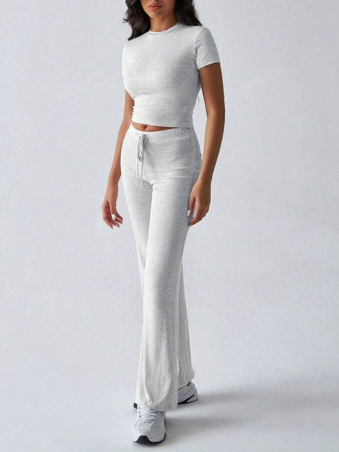 Person wearing a white crop top and light gray flared pants on a plain background