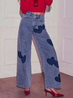 Person wearing blue jeans with heart patterns and a red top against a white paneled wall.