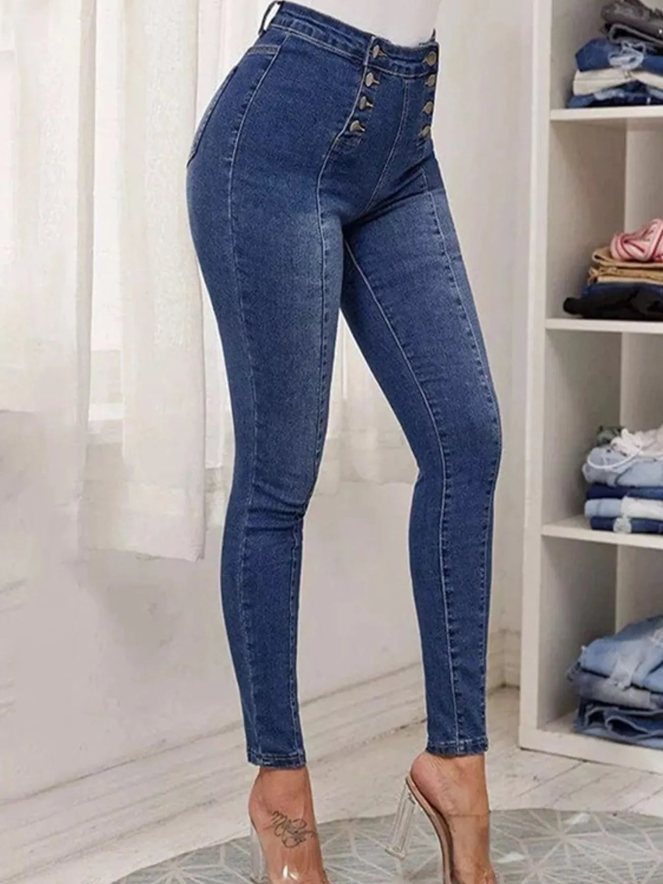 Blue jeans worn by a person in a room with shelves and clothes.