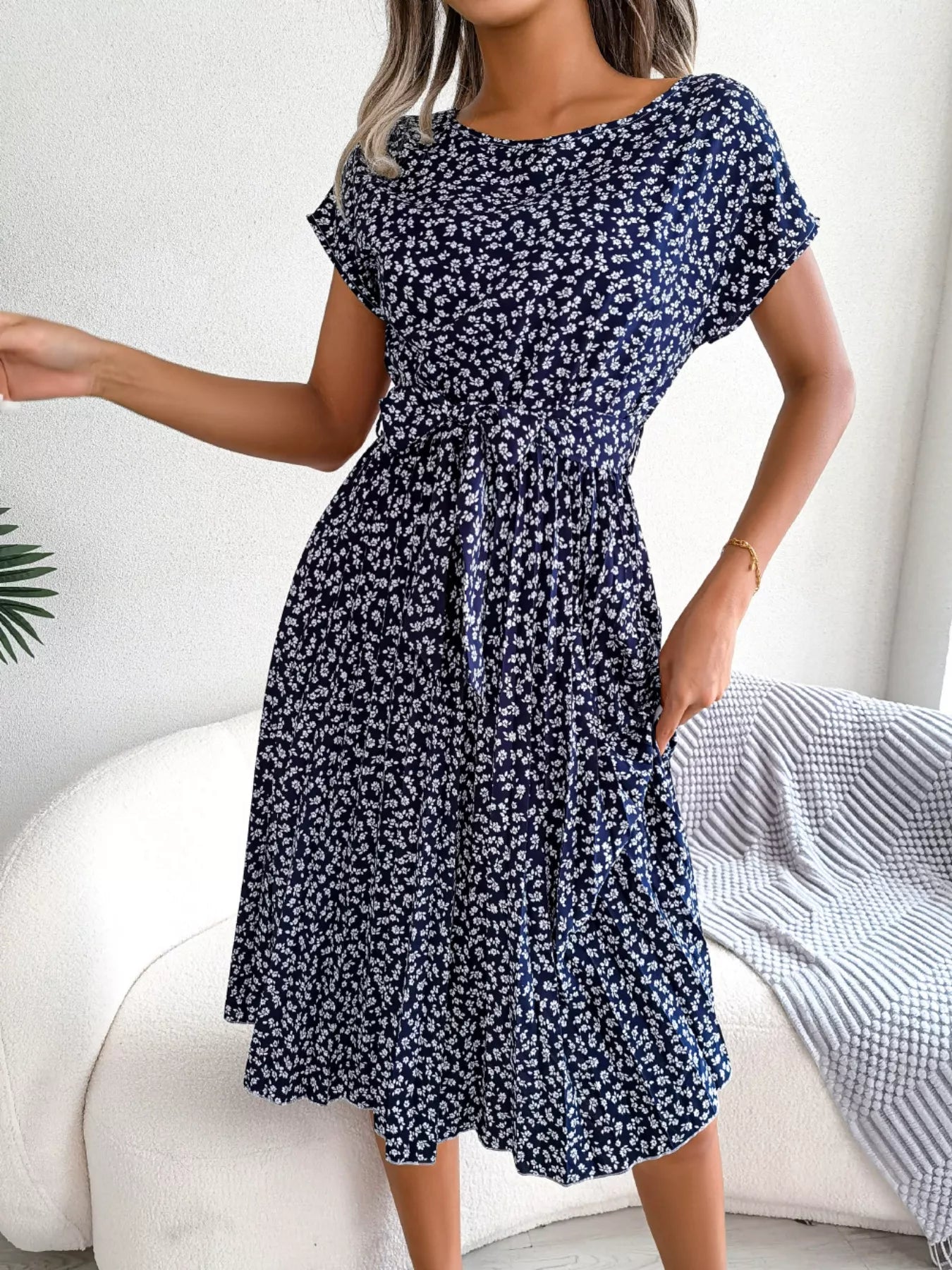 Woman wearing a navy floral dress sitting on a white couch.