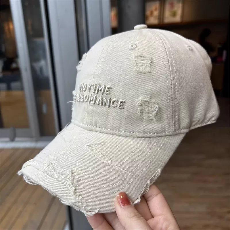 Beige distressed baseball cap with text held by a hand indoors.