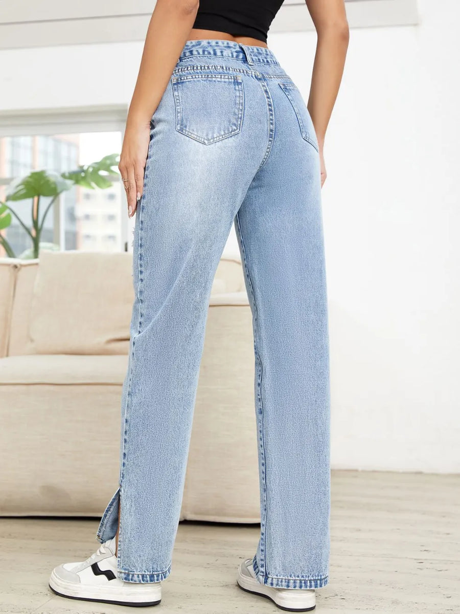 Person wearing light blue jeans in a room with a couch and plants.
