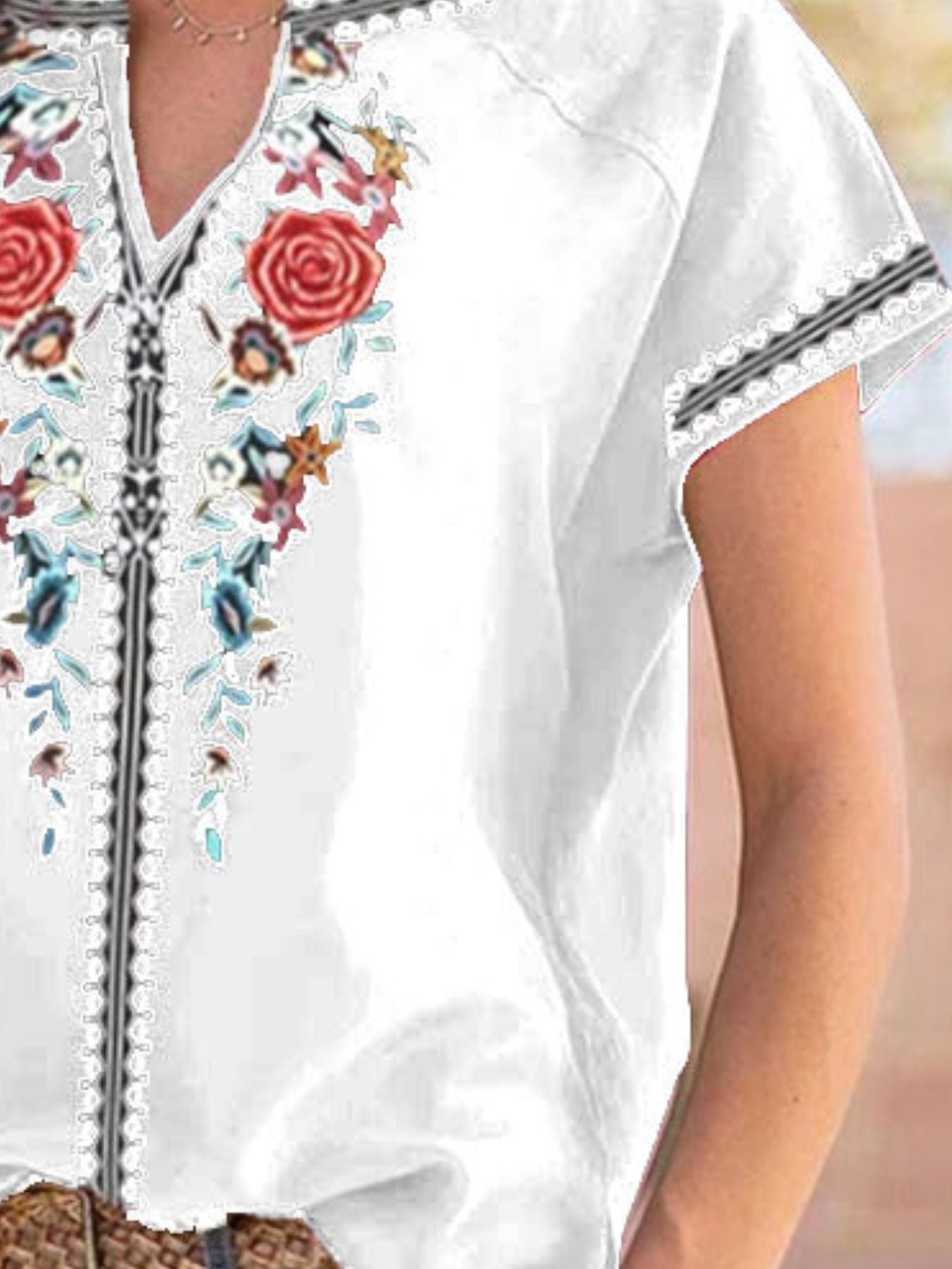 White blouse with colorful floral embroidery and black trim on a neutral background