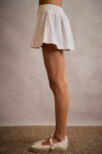 Person wearing a white skirt and beige shoes on a neutral background