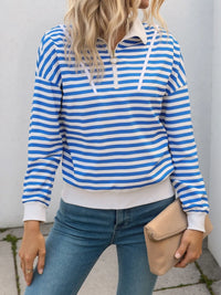 Person wearing a blue and white striped hoodie with jeans and holding a beige clutch.