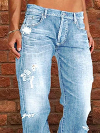 Blue jeans with distressing details worn by a person against a brick wall.