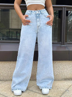 Person wearing light blue wide-leg jeans and white sneakers on a city street.