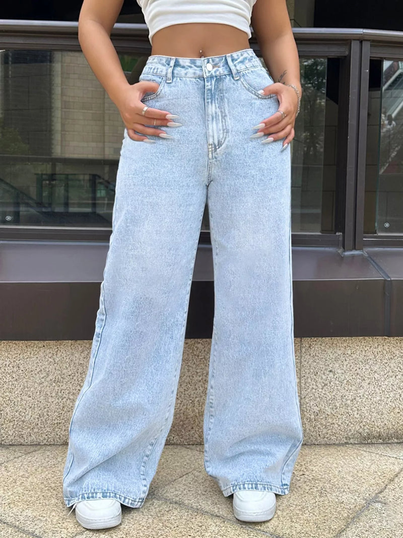 Person wearing light blue wide-leg jeans and white sneakers on a city street.