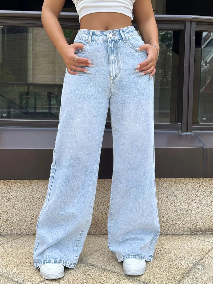Person wearing light blue wide-leg jeans and white sneakers on a city street.
