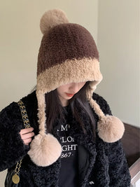 Person wearing a brown and beige two-tone fur hat with pom-poms.