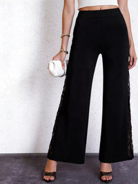 Person wearing black wide-leg pants with lace details on a plain background
