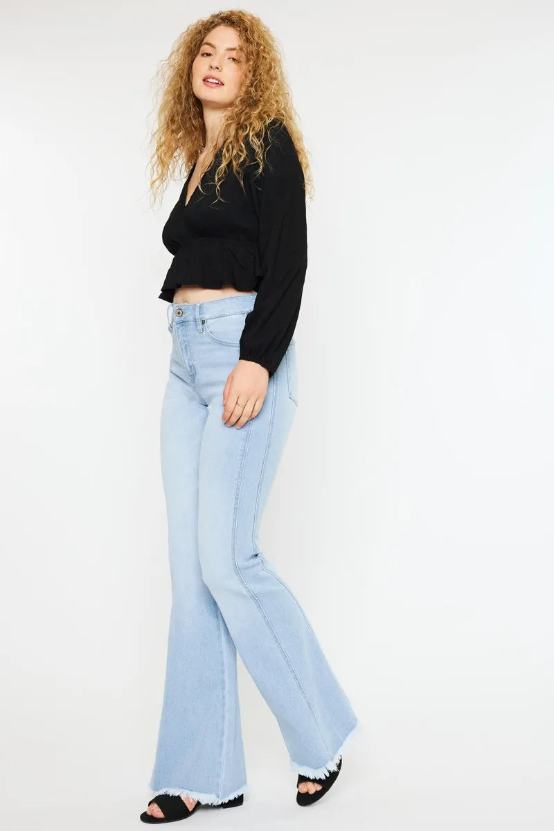 Woman wearing a black top and light blue flared jeans on a white background