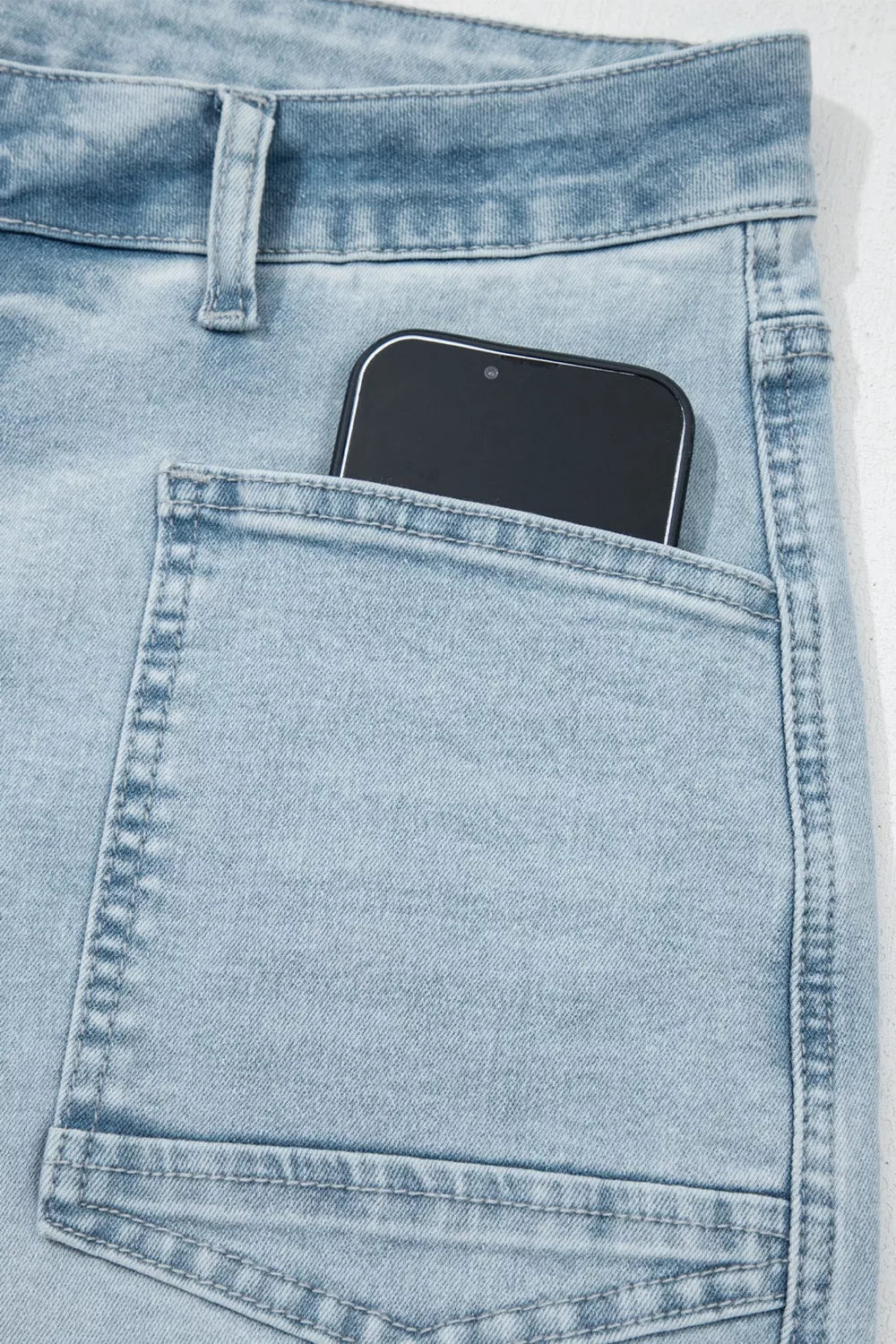 Light blue denim jeans with a smartphone in the pocket on a white background