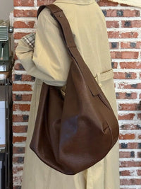 Person wearing a brown leather bag against a brick wall.