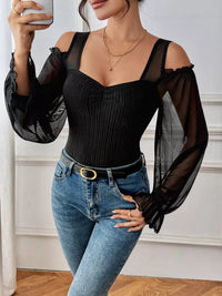 Woman wearing a black ribbed top with sheer sleeves and blue jeans indoors.