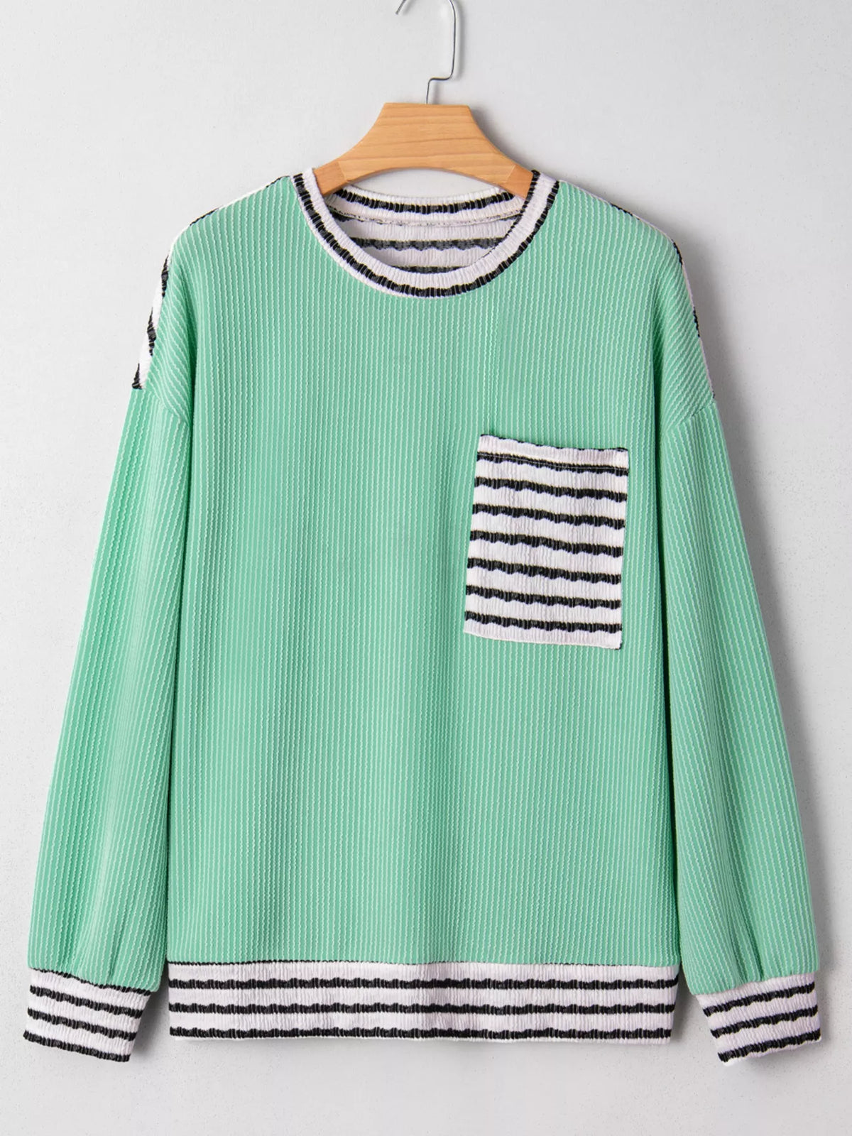 Green sweater with striped details on a wooden hanger against a white background
