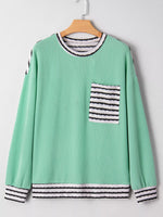 Green sweater with striped details on a wooden hanger against a white background