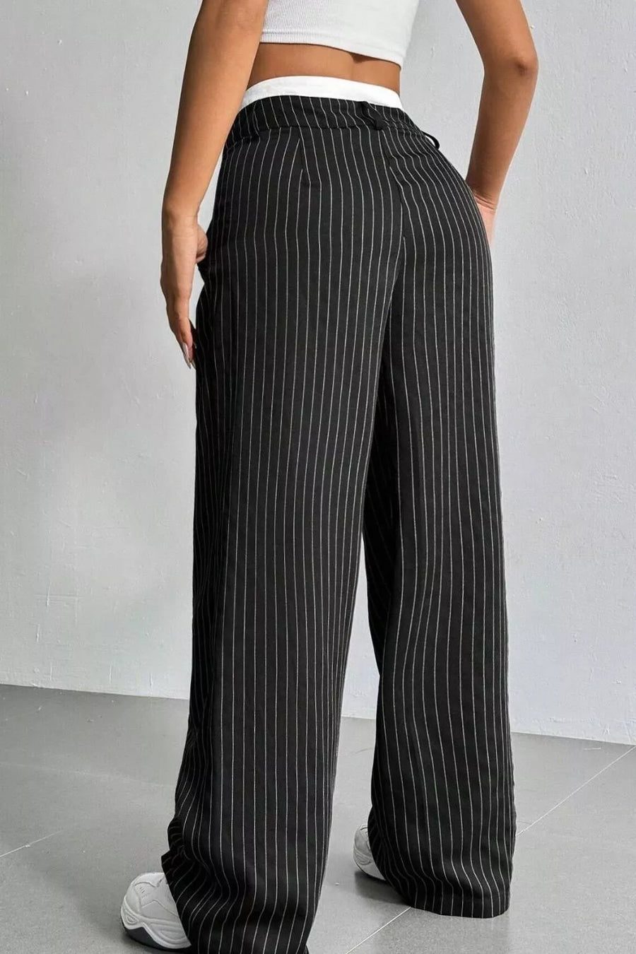 Black wide-leg pinstripe trousers with a drawstring waist, shown on a model from the back against a light gray studio background.