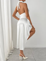 Woman wearing a white dress with a slit, standing in a room with white curtains and walls.