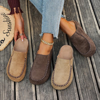 Brown and beige loafers on a wooden floor with a person wearing jeans.