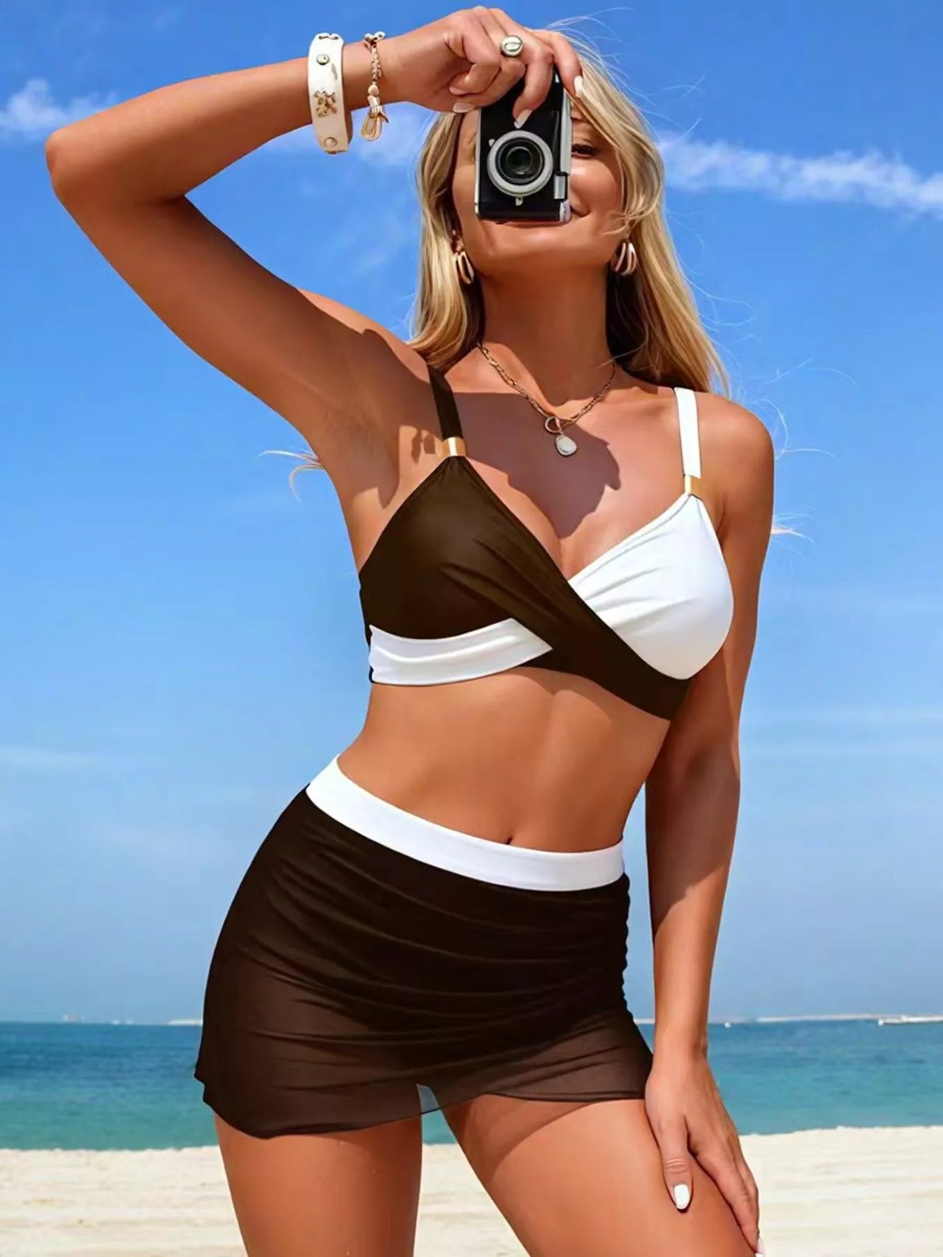 Woman in a brown and white bikini taking a selfie on a beach.