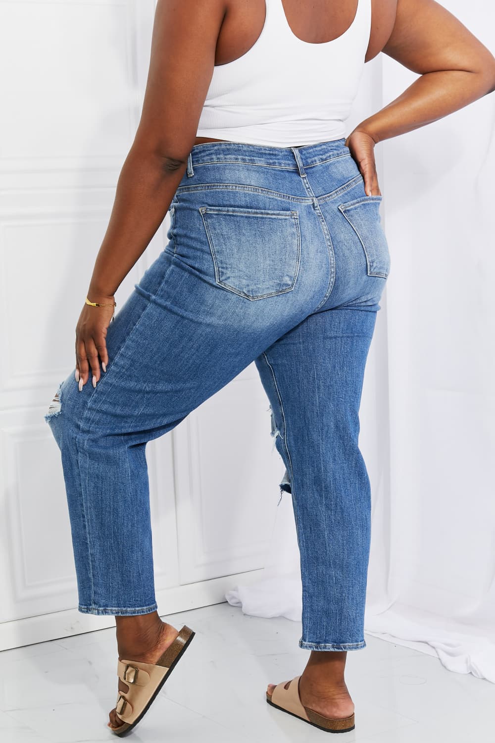 Person wearing blue jeans and a white tank top against a white background