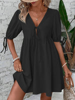 Woman wearing a black dress with puff sleeves against a white brick wall.