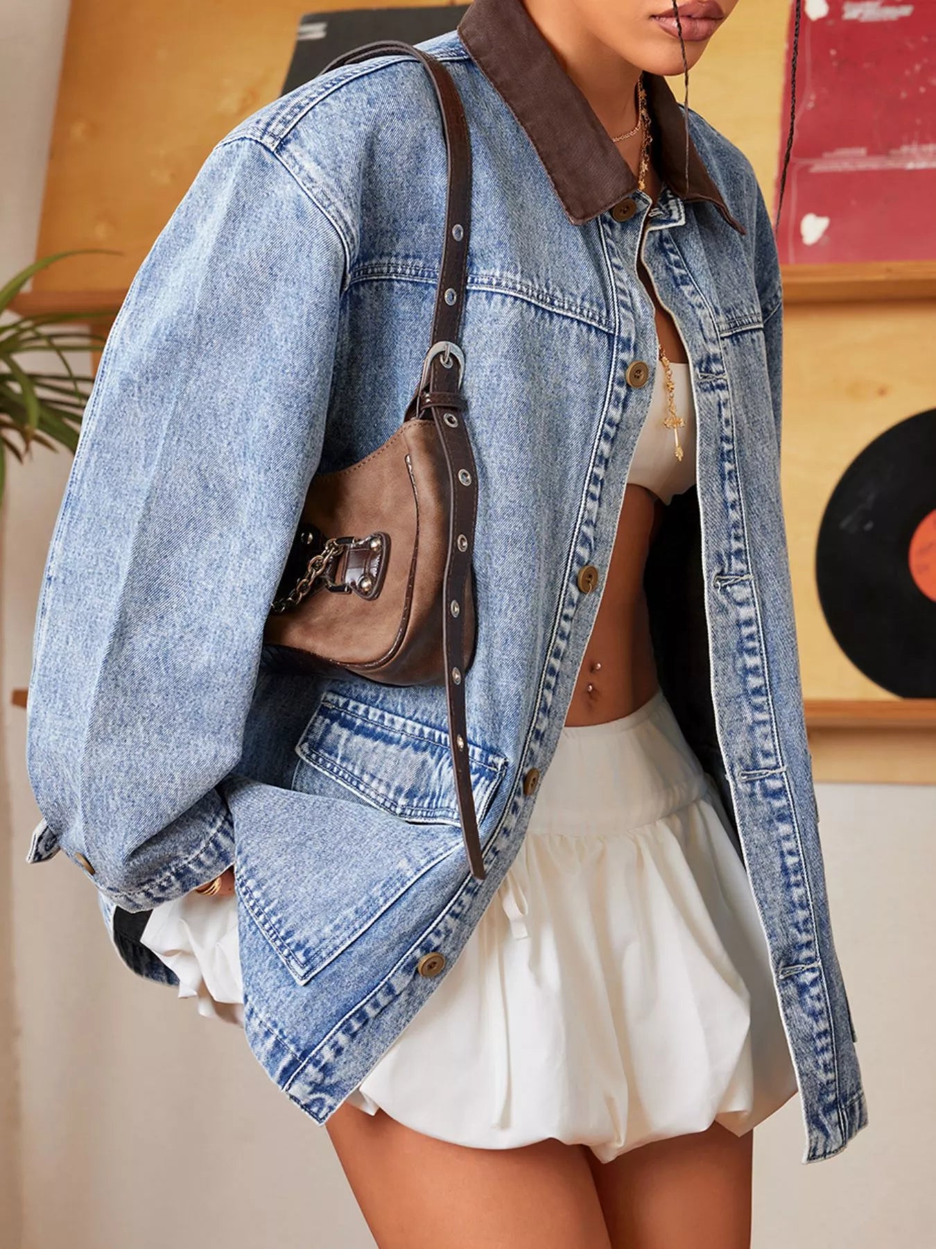 Person wearing a denim jacket over a white top and skirt, holding a brown bag.
