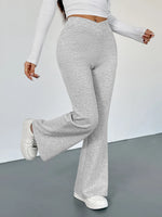 Person wearing gray flared pants and white long-sleeve top on a plain background