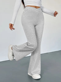 Person wearing gray flared pants and white long-sleeve top on a plain background