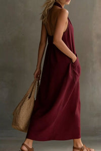 Woman in a burgundy dress holding a woven bag against a neutral background