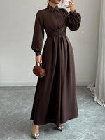 Woman wearing a brown dress holding a matching handbag indoors.