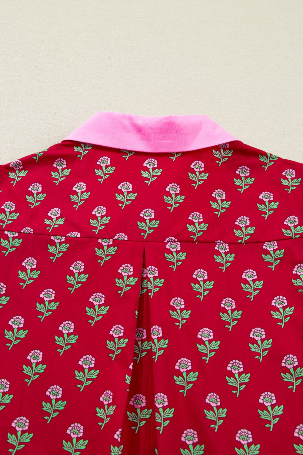 Red garment with floral pattern and pink collar on a beige background
