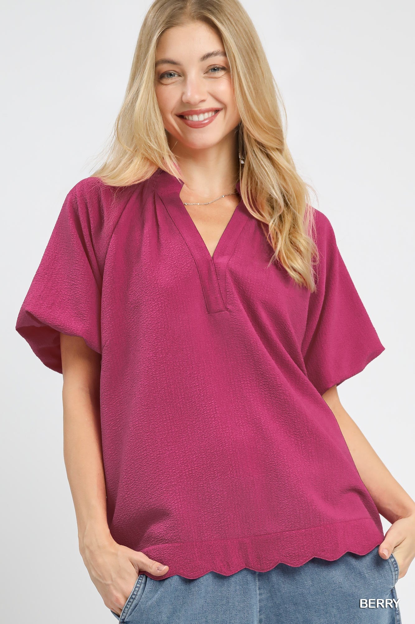 Woman wearing a magenta top with scalloped hem on a white background