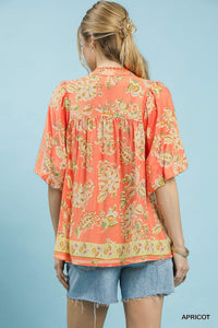Woman wearing a coral floral blouse with denim shorts on a light blue background