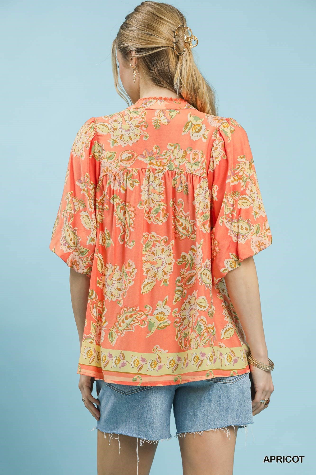 Woman wearing a coral floral blouse with denim shorts on a light blue background