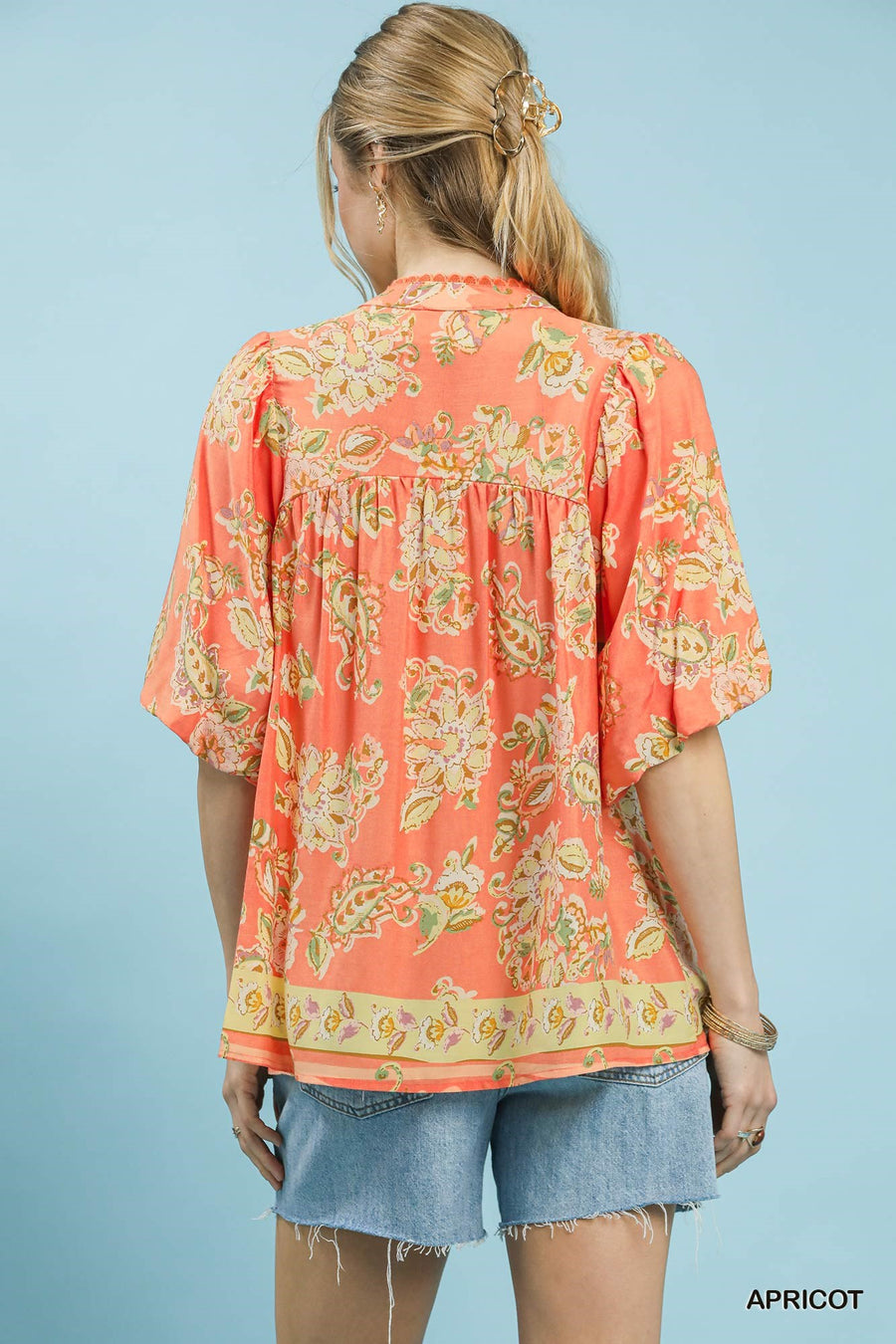 Woman wearing a coral floral blouse with denim shorts on a light blue background