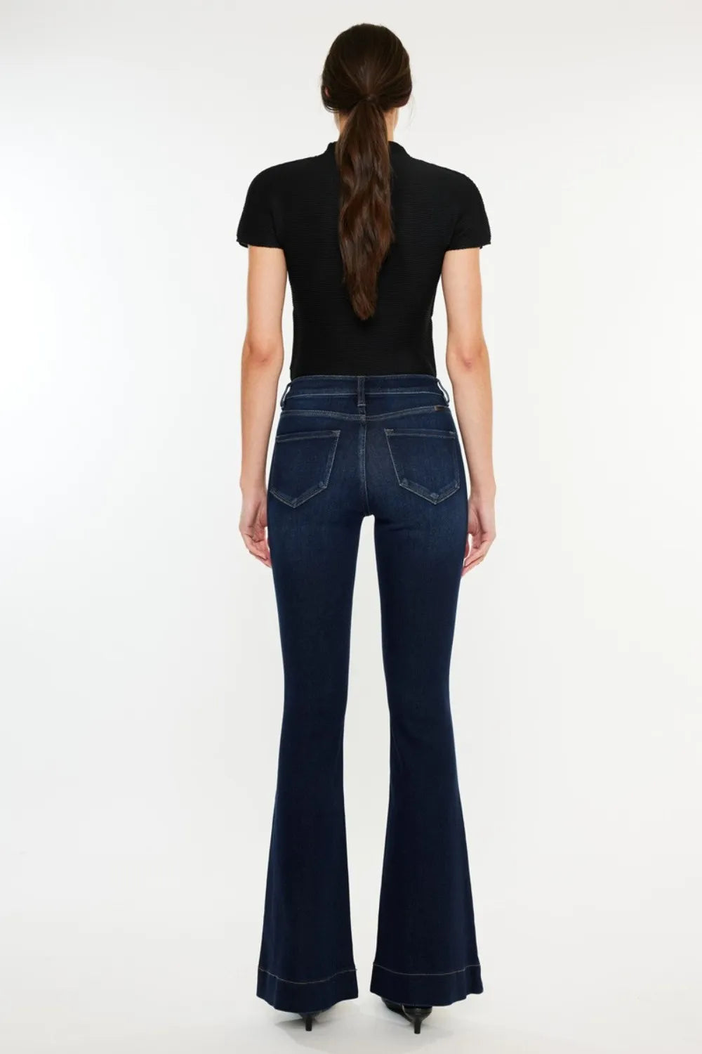 Person wearing dark blue flared jeans on a white background