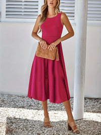 Woman wearing a pink dress holding a brown clutch against a white wall.