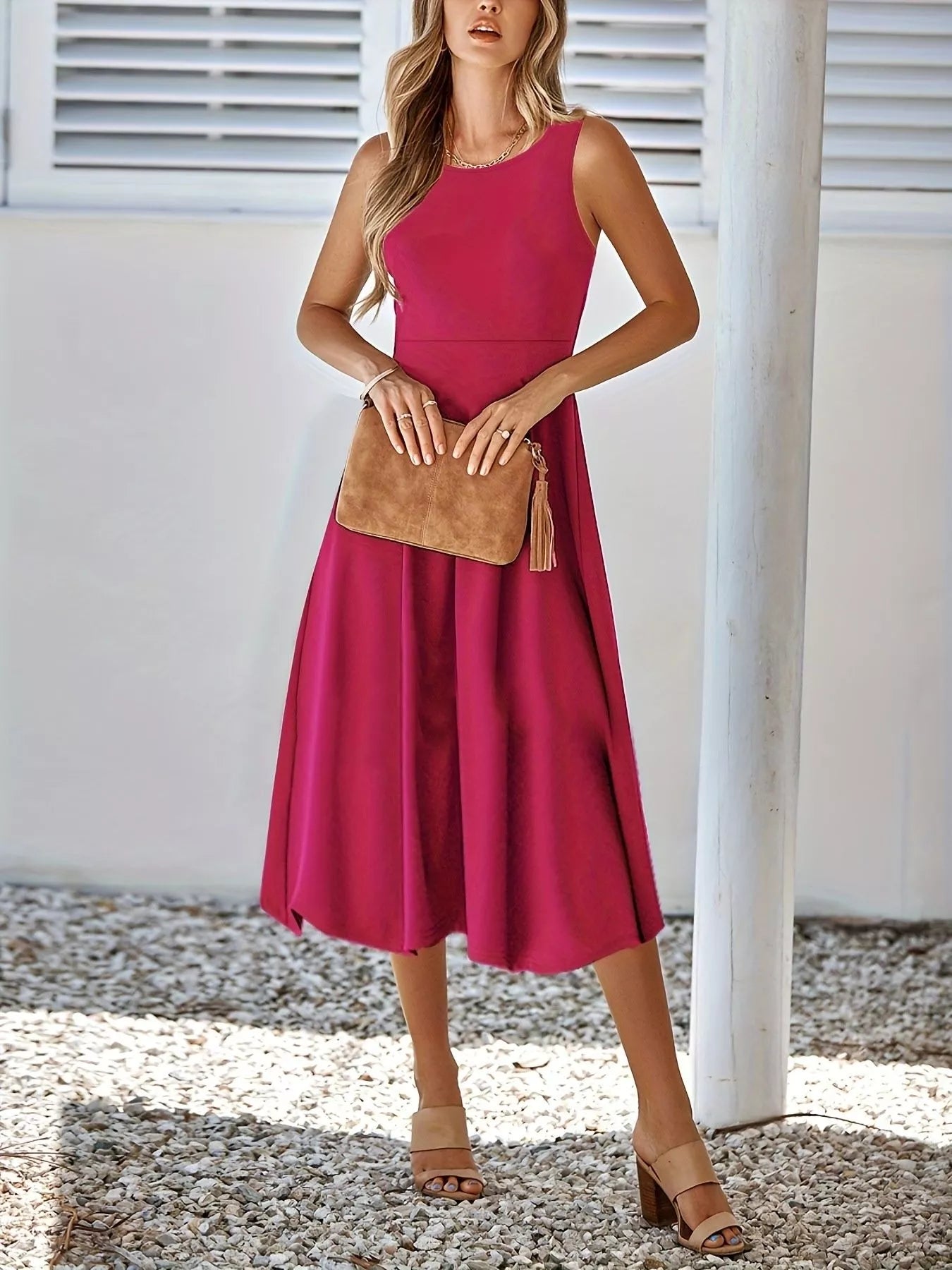 Woman wearing a pink dress holding a brown clutch against a white wall.